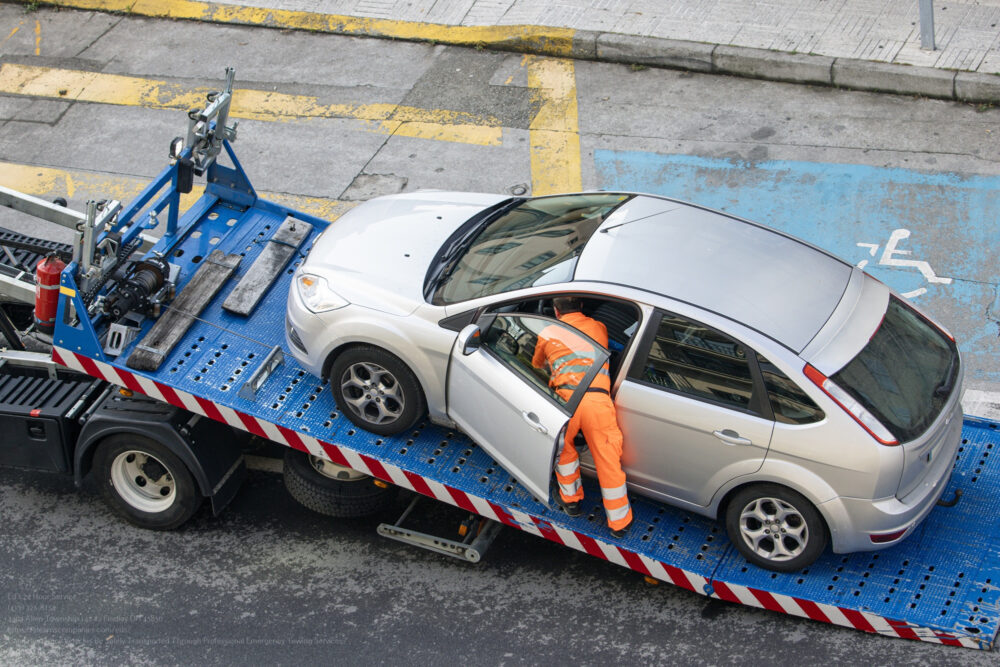 Damaged Car Being Loaded Onto Tow Truck By A Worker. Towing Serv